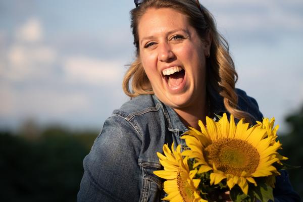 A WOMAN SMILES HOLFING A SUNFLOWER